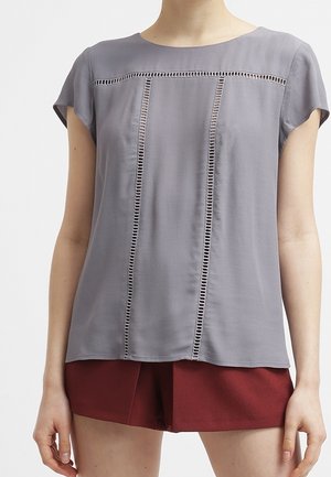 Graue Bluse mit kurzen Ärmeln, die vertikale Ausschnittdetails entlang der Vorderseite aufweist. Weicher, glatter Stoff mit lockerer Passform.