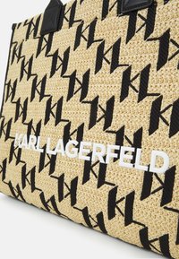 Vävd halmtrådkasse med ett svart geometriskt mönster, läderdetaljer och en iögonfallande vit "KARL LAGERFELD"-logotyp på framsidan.