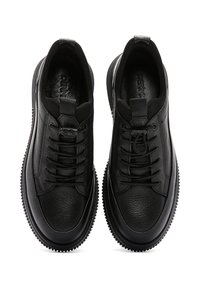 Black sneakers featuring a textured leather upper, lace-up design, and a smooth rubber sole with a ridged edge.