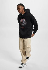 Sudadera negra con diseño gráfico que presenta una cara y acentos rojos. Combinada con pantalones cargo beige y zapatillas en blanco y negro.