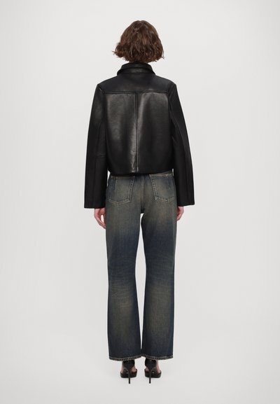 Svart läderjacka med kort längd och hög krage, tillsammans med urblekta vida jeans med råa sömmar och subtila tvättvariationer.