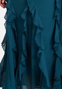 Abito teal con strati arricciati lungo l'orlo, realizzato in tessuto leggero, con una consistenza morbida e trasparente e una silhouette fluida.