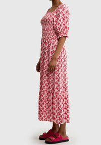 Ruokapuku maksimekko vaaleanpunaisena, jossa on puffihihat, smockattu yläosa ja kerroksellinen hame; yhdistetty kirkkaanpunaisiin liu'uttaviin sandaaleihin.