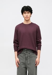 Głęboko fioletowy sweter z długim rękawem i okrągłym dekoltem, wykonany z teksturowanej tkaniny, zestawiony z jasnoszarymi spodniami z wiązaniem w talii.