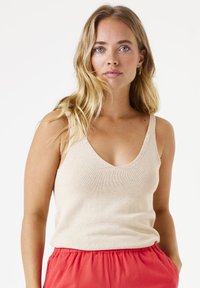 Top sin mangas de punto beige con escote en V profundo y tirantes anchos, combinado con pantalones cortos de cintura elástica en color coral. Textura suave y diseño casual.