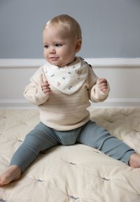 Εφαρμοστή κρεμ ζακέτα με ριγέ υφή, ανοιχτό μπλε ριγέ κολάν και μπουφάν με μοτίβο. Καθισμένο σε μια ραμμένη επιφάνεια σε ουδέτερους τόνους.