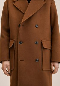 Manteau en laine marron à double boutonnage, avec de grands boutons noirs et deux poches avant à rabats. Texture lisse avec de larges revers.