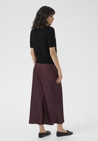 Black short-sleeve top paired with a long, burgundy skirt. The skirt is smooth with a slight sheen and finished with a flowing hem. Black flats.