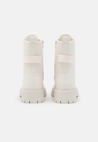 Weiße Knöchelstiefel mit einer glatten Lederstruktur, ausgestattet mit einem seitlichen Reißverschluss, elastischen Riemen und einem stabilen Blockabsatz mit einer gemusterten Sohle.