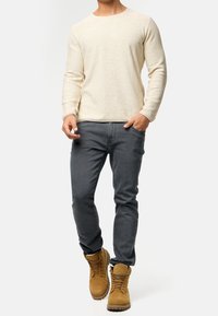 Pull en tricot beige clair, jean gris slim-fit et bottes à lacets marron clair avec une surface texturée. Design simple et classique avec des tons neutres.