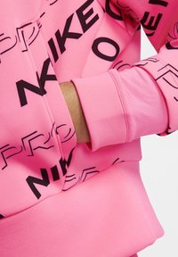 Felpa rosa con una texture morbida e il noto marchio Nike in evidenza. Ingrandimento della manica con dettagli visibili sui polsini e sulle cuciture.
