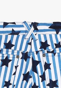 Niebiesko-biały materiał w paski, ozdobiony czarnymi gwiazdami, z widocznym guzikiem i haftowanym pikowaniem w kształcie X przy pasie. Materiał dżinsowy.