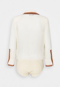 Vit blus med brun krage och manschetter. Slät textur med långa ärmar. Enkelt design, utan synliga knäppningar eller mönster.