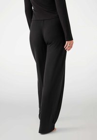 Black wide-leg pants made from soft fabric, featuring a smooth texture and a relaxed fit. The model is shown from the back, barefoot.