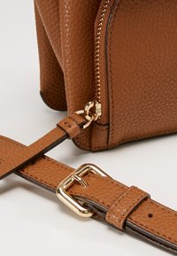Borsa in pelle marrone con texture e cerniera dorata, dotata di una tracolla rimovibile con fibbia rettangolare e finitura liscia.