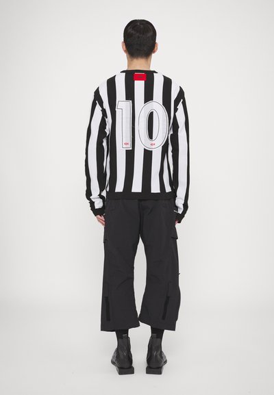 Schwarz-weißer gestreifter Langarmshirt mit der Nummer "10" auf dem Rücken, kombiniert mit schwarzen Cargo-Hosen und Stiefeletten.