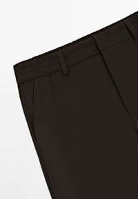 Mørkebrune bukser med elastisk talje, glat tekstur, skræddersyet design og sidelommer. Ensfarvet mønster uden yderligere detaljer.