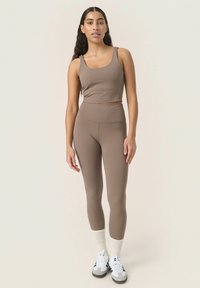 Bruine crop top en high-waisted leggings, gemaakt van gladde stof. Het model draagt witte sokken en schoenen met grijze accenten.