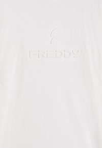 Camiseta blanca de algodón con una textura suave, que presenta un logo blanco en relieve "FREDDY" en el centro y un acento curvado encima del logo.