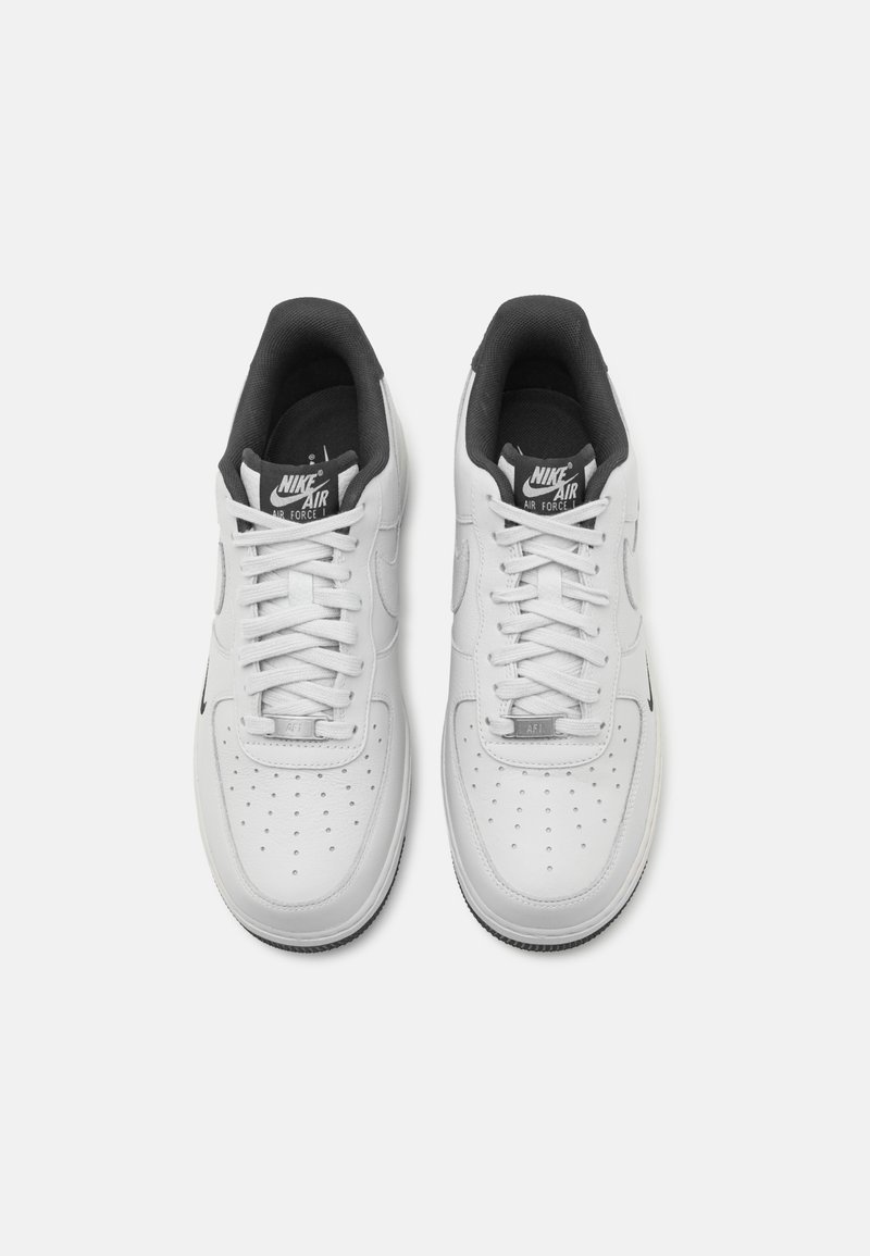 Białe sneakersy Nike Air Force 1 z gładką skórzaną cholewką, okrągłym czubkiem, perforowanymi detalami oraz czarnymi akcentami na języku i podeszwie.