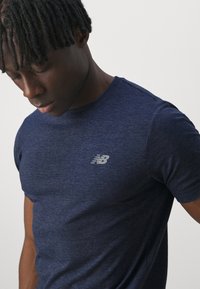 T-shirt de sport bleu marine en tissu doux et texturé, avec un petit logo gris sur la poitrine et un col ras du cou classique.