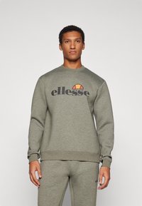 Maslinasto zeleni dukserica s rebrastim manžetama i rubom, s velikim crnim logotipom "ellesse" i šarenom polukružnom grafikom.