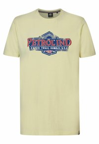 Světle žluté bavlněné tričko s grafickým potiskem "PETROL IND" v červené a modré barvě, umístěné na vintage stylovém designu štítku.