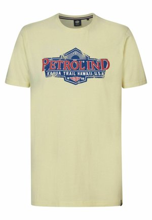 Lichtgele katoenen T-shirt met een grafische print van "PETROL IND" in rood en blauw, tegen een vintage-stijl labelontwerp.