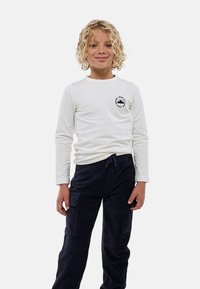 Chemise blanche à manches longues avec un motif de montagne sur la poitrine, associée à un pantalon en velours côtelé bleu marine doté de poches latérales et d'une taille à cordon.