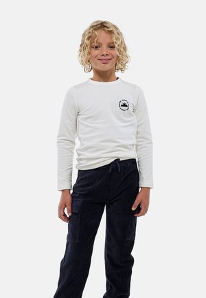 Chemise blanche à manches longues avec un motif de montagne sur la poitrine, associée à un pantalon en velours côtelé bleu marine doté de poches latérales et d'une taille à cordon.