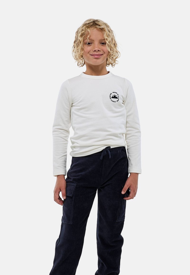 Chemise blanche à manches longues avec un motif de montagne sur la poitrine, associée à un pantalon en velours côtelé bleu marine doté de poches latérales et d'une taille à cordon.