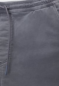 Szare spodnie dresowe wykonane z miękkiego materiału, z elastycznym pasem oraz sznurkiem do regulacji, a także bocznymi kieszeniami. Gładka tekstura i brak widocznych wzorów.