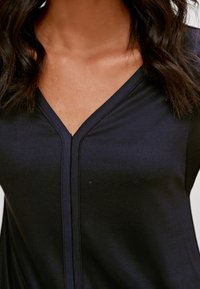 Top blu navy con scollo a V, realizzato in tessuto morbido. Presenta un dettaglio di cucitura centrale lungo la linea del collo. Tessuto liscio.