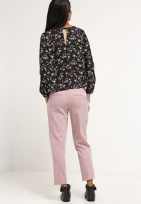 Blusa nera floreale con maniche lunghe e dettaglio a chiave sulla schiena, abbinata a pantaloni rosa slim-fit e stivali alla caviglia con fibbie.