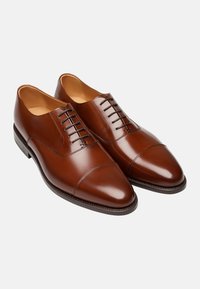 Bruine leren dresschoenen met een gladde afwerking, cap toe ontwerp en zes gaatjes voor veters. De buitenzool heeft een subtiele profiel voor grip.