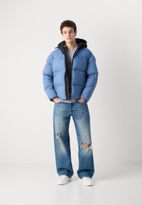 Blue puffer jacket with a black interior and hood, paired with distressed light blue wide-leg jeans and white sneakers.