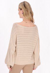 Pulover tricotat bej cu mâneci largi, tip batwing, având un guler larg și un model texturat cu dungi orizontale.