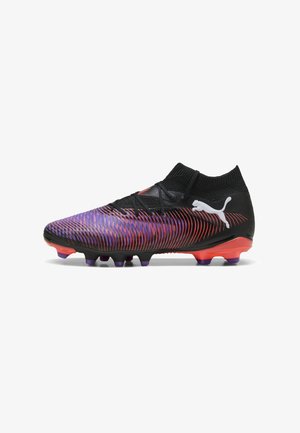 Botas de fútbol negras con una superficie texturizada que presenta franjas degradadas en púrpura y rojo, diseño de tobillo bajo y un logo blanco audaz.