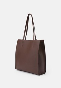 Brązowa skórzana torba typu tote o gładkiej fakturze, z przeszyciami bocznymi i płaskimi ramiączkami. Prostokątny kształt z wyraźnie zarysowanym designem.
