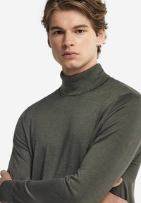 Grå polotröja gjord av ett mjukt, texturerat tyg. Har långa ärmar och en figurnära design, med ribbad halsringning och ärmslut.