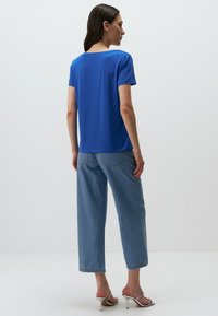 Niebieska koszulka z krótkim rękawem wykonana z miękkiego materiału, połączona z jasnoniebieskimi, szerokimi dżinsami. Widok z tyłu pokazuje prosty, klasyczny krój i luźny fason.