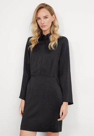 Schwarzes, langärmliges Kleid aus glattem Stoff mit einem geknöpften Kragen und tailliertem Schnitt, das bis zur Mitte des Oberschenkels gerade geschnitten ist.