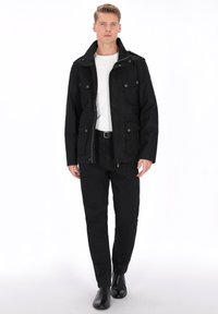 Sort jakke med justerbar krave, forlommer og lynlåslukning; båret over en hvid skjorte og kombineret med sorte bukser og støvler.