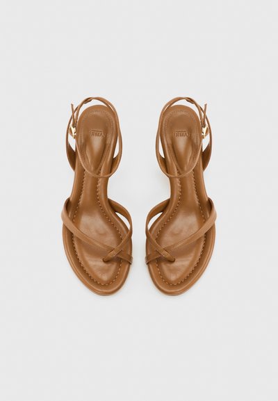 Καφέ δερμάτινα σανδάλια με λεπτά λουράκια που διασταυρώνονται πάνω από τα δάχτυλα και λουριά με αγκράφα στον αστράγαλο, απεικονίζονται από πάνω σε απλό φόντο.