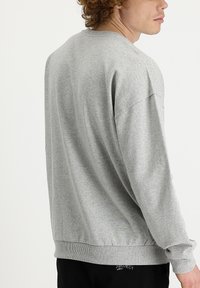 Sudadera gris con cuello redondo, corte relajado, puños y cinturilla acanalados. Los materiales parecen suaves con una sutil textura jaspeada.