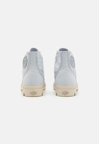 Botines de lona azul claro con un acento de logo redondo en el talón y una suela de goma beige, que presenta un patrón texturizado.