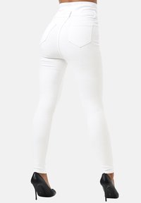 Jeans blancos ajustados de cintura alta, con una textura suave, dos bolsillos traseros y combinados con zapatos de tacón altos negros.