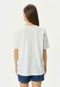 Camiseta blanca de algodón con mangas cortas, escote redondo y un corte holgado, combinada con pantalones cortos de mezclilla azules. Sin patrones ni acentos visibles.
