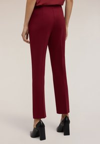 Bordové kalhoty na míru se slim fit, s hladkou texturou a středně vysokým pasem. Černé boty na blokovém podpatku doplňují vzhled.