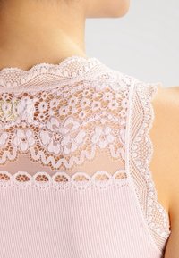 Ljust rosa topp med utsökt spetsdetalj på ryggen, scalloped kanter och en texturerad räfflad tyg.